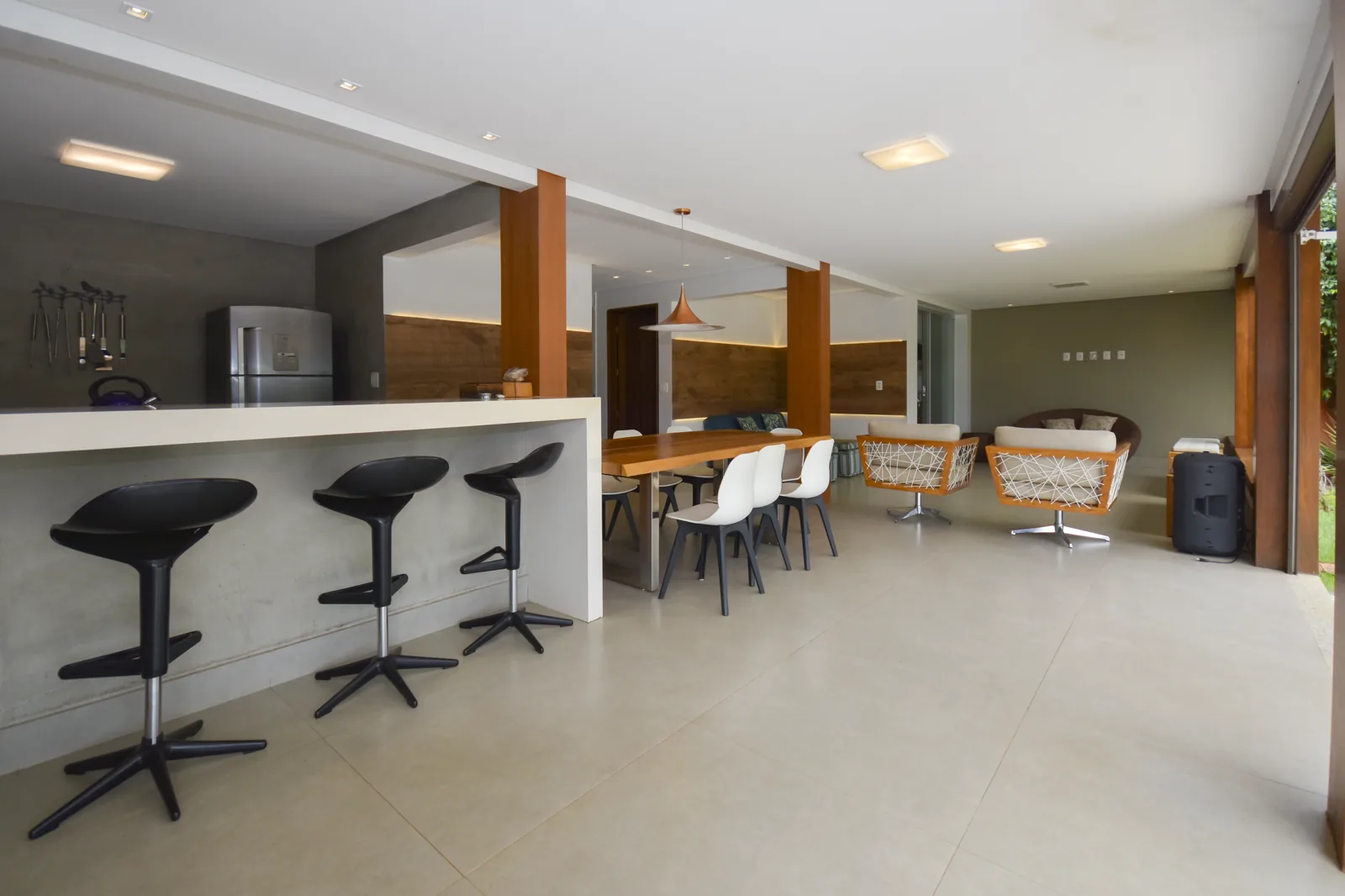 Espaço gourmet com bancada de concreto, banquetas e poltronas swivel